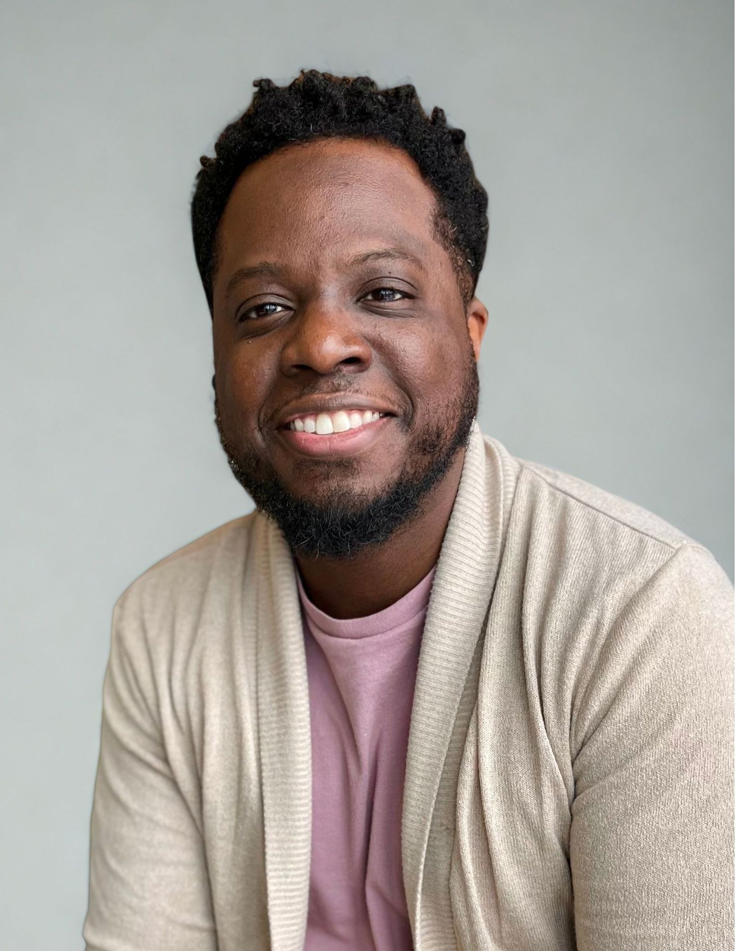 Person wearing a light beige cardigan and a pink shirt against a neutral gray background.