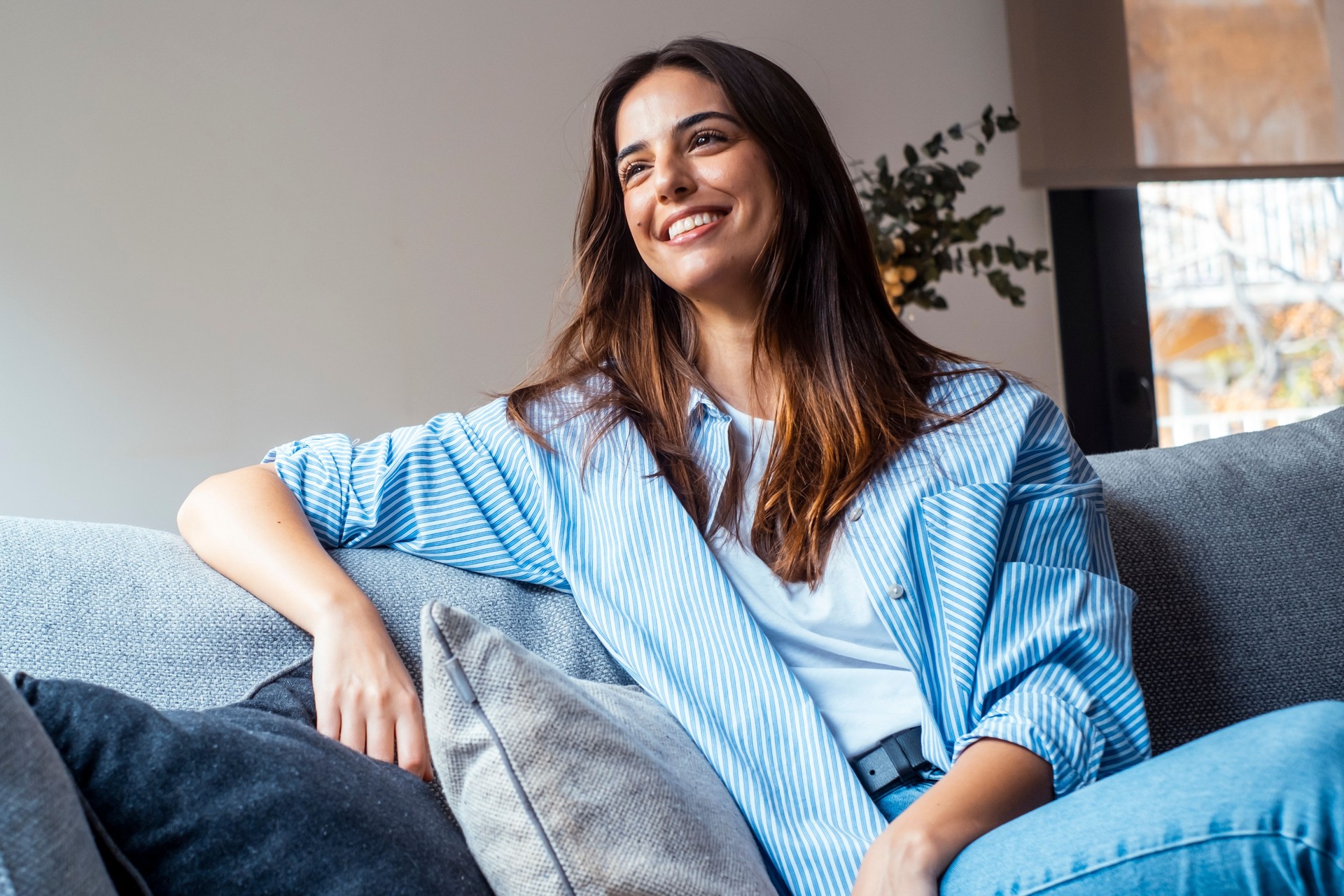 Relax and unwind. Young beautiful brunette woman with blissful facial expression smiles alone on the sofa. Portrait of relaxed woman resting at home.